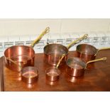A SET OF SIX EARLY 20TH CENTURY COPPER PANS, with brass hooped handles
