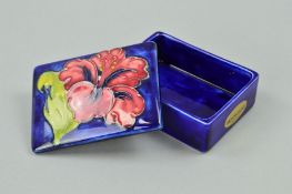 A SMALL MOORCROFT POTTERY RECTANGULAR COVERED POT, 'Hibiscus' pattern on blue ground, impressed