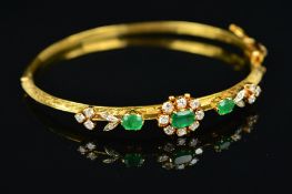 A MID 20TH CENTURY 18CT GOLD EMERALD AND DIAMOND HALF HOOP BANGLE, centring on an emerald and