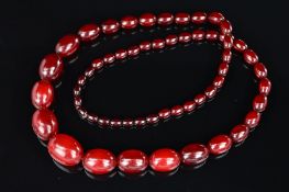 A LONG RED PLASTIC BEAD NECKLACE, designed as graduated barrel shape beads measuring 10mm to 28mm,