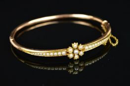 A GOLD EARLY 20TH CENTURY SEED PEARL HALF HOOP BANGLE, centring on a flower, flanked by seed