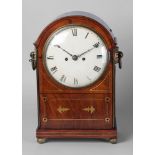 A Regency mahogany and brass inlaid mantel clock, the case with an arched top and ring form carrying
