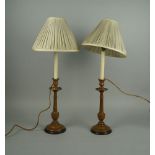 A pair of turned wood candlestick type lamp bases, with pleated cream material shades, 69cm high