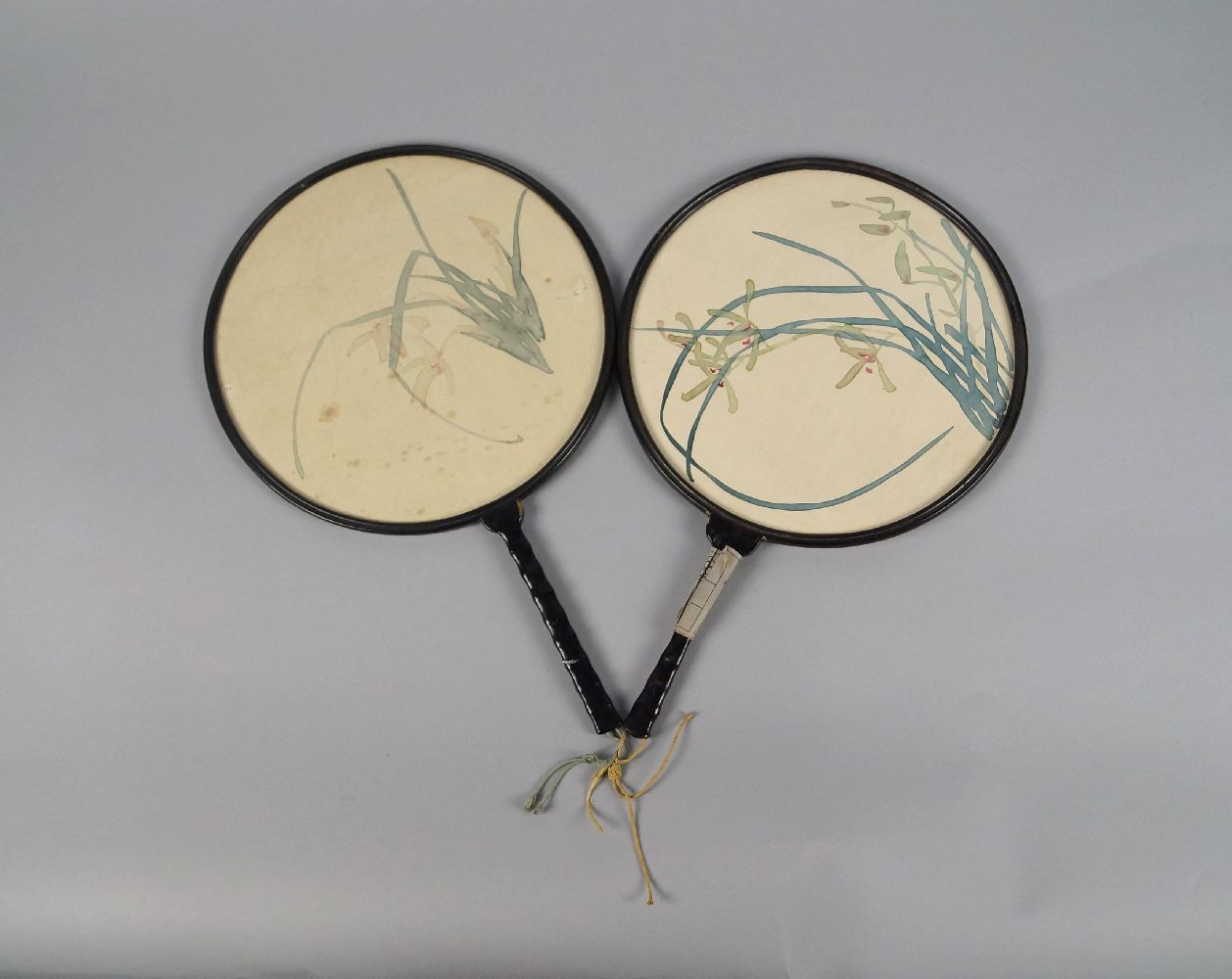 A pair of Chinese fans, 20th century, of circular form, the leaves painted with orchids on silk,