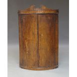 A George III oak and cross-banded bow fronted corner cupboard, with broken swan neck pediment