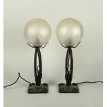 A pair of wrought iron and glass lamps, 20th century, the globular shades of crackle glass form,