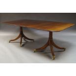 A George III style mahogany twin pedestal dining table, the rectangular top above two turned columns