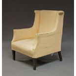 An Edwardian wingback armchair, upholstered in cream fabric, on square tapering legs