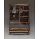 An oak bookcase, early 20th Century, with two glazed doors enclosing three shelves, on turned legs