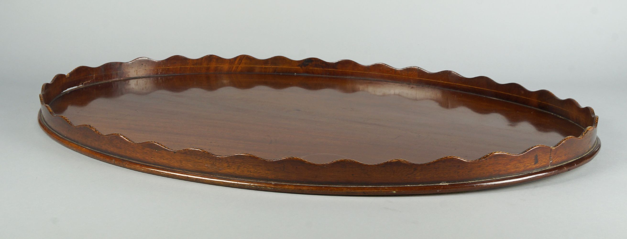 A large oval mahogany tray, late 19th/early 20th century, with a wavy edged gallery inset with
