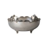 A white metal bowl, of circular form, the shaped rim with moulded scroll border, raised on four