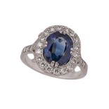 A French white gold, sapphire and diamond cluster ring, the cushion-shaped sapphire weighing
