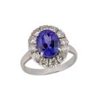 An 18ct. gold, tanzanite diamond cluster ring, the claw-set oval tanzanite with circular-cut diamond