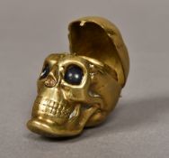 A Victorian brass novelty sovereign holder Formed as a skull, the nose forming the catch release,