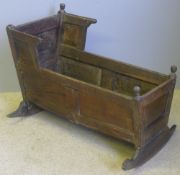 An 18th century oak crib Of panelled form, with turn finials and shaped rockers. 95 cm long.