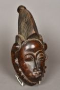 An African tribal carved wooden mask Formed with elongated hair, eye slits and scarified face.