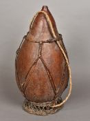 An African tribal water carrier Formed from a large gourd with a basket weave framework and rope