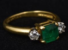 An 18 ct gold diamond and emerald ring The central claw set square emerald flanked by two diamonds.
