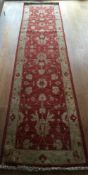 A wool runner, the red field with floral motifs and within a cream border.