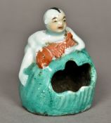 A Chinese porcelain brush washer Modelled as a young boy holding a fish, climbing a boulder.