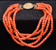 An unmarked 18 ct gold mounted coral necklace Of five strand form, with a domed gold filigree clasp.