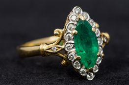 An 18 ct gold, diamond and emerald cluster ring Of marquise shape with pierced scrolling shoulders.