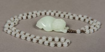 A Chinese carved mutton fat jade pendant and bead necklace The pendant worked as a mythical beast.