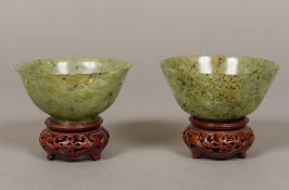 A pair of Chinese carved green and russet jade bowls Standing on carved and pierced wood bases.