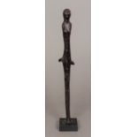 A stylised bronze female figure Of elongated form, standing on a slate plinth base.