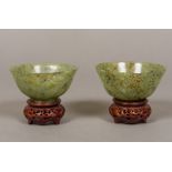 A pair of Chinese carved green and russet jade bowlsm standing on carved and pierced wood bases.
