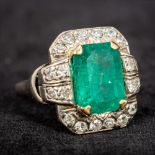 An unmarked white gold or platinum emerald and diamond ring The central claw set emerald bordered