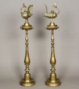 A pair of large Indian brass oil lamps Each surmounted with a peacock,