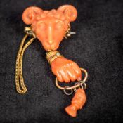 A 19th century unmarked gold mounted coral brooch Formed as a ram's mask above a clenched hand