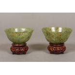 A pair of Chinese carved green and russet jade bowls standing on carved and pierced wood bases.