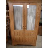 Waxed pine wardrobe enclosed by two glazed and panelled cupboard doors (width 113cm)