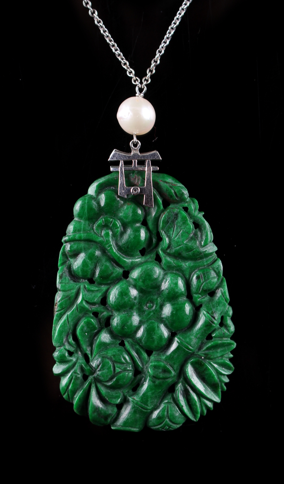 A Chinese carved untreated jadeite pendant depicting flowers & bamboo, the white metal mount with