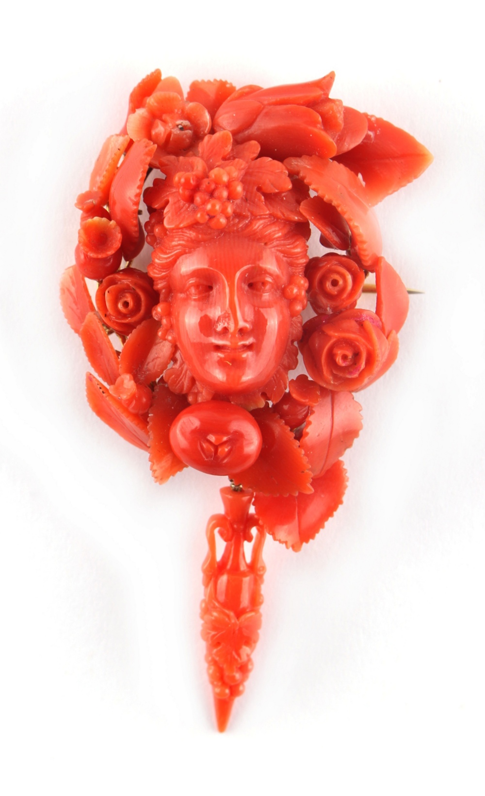 A carved coral brooch modelled as a Bacchanalian mask framed by fruit, flowers & leaves, with