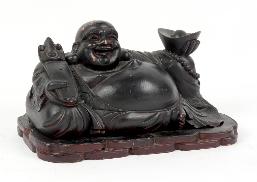 A Chinese carved & black painted wood figure of Budai, modelled recumbent & holding a ruyi