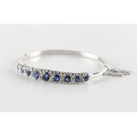An early 20th century sapphire & diamond hinged bangle, the nine well matched graduated oval cut
