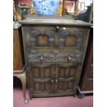 A Reprodux Oak Drinks Cabinet, with butterfly hinges, arched panels to fall front, scroll carved