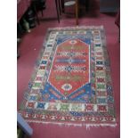 A Middle Eastern Wool Rug, with bar of five geometric motifs within hexagonal red centre and