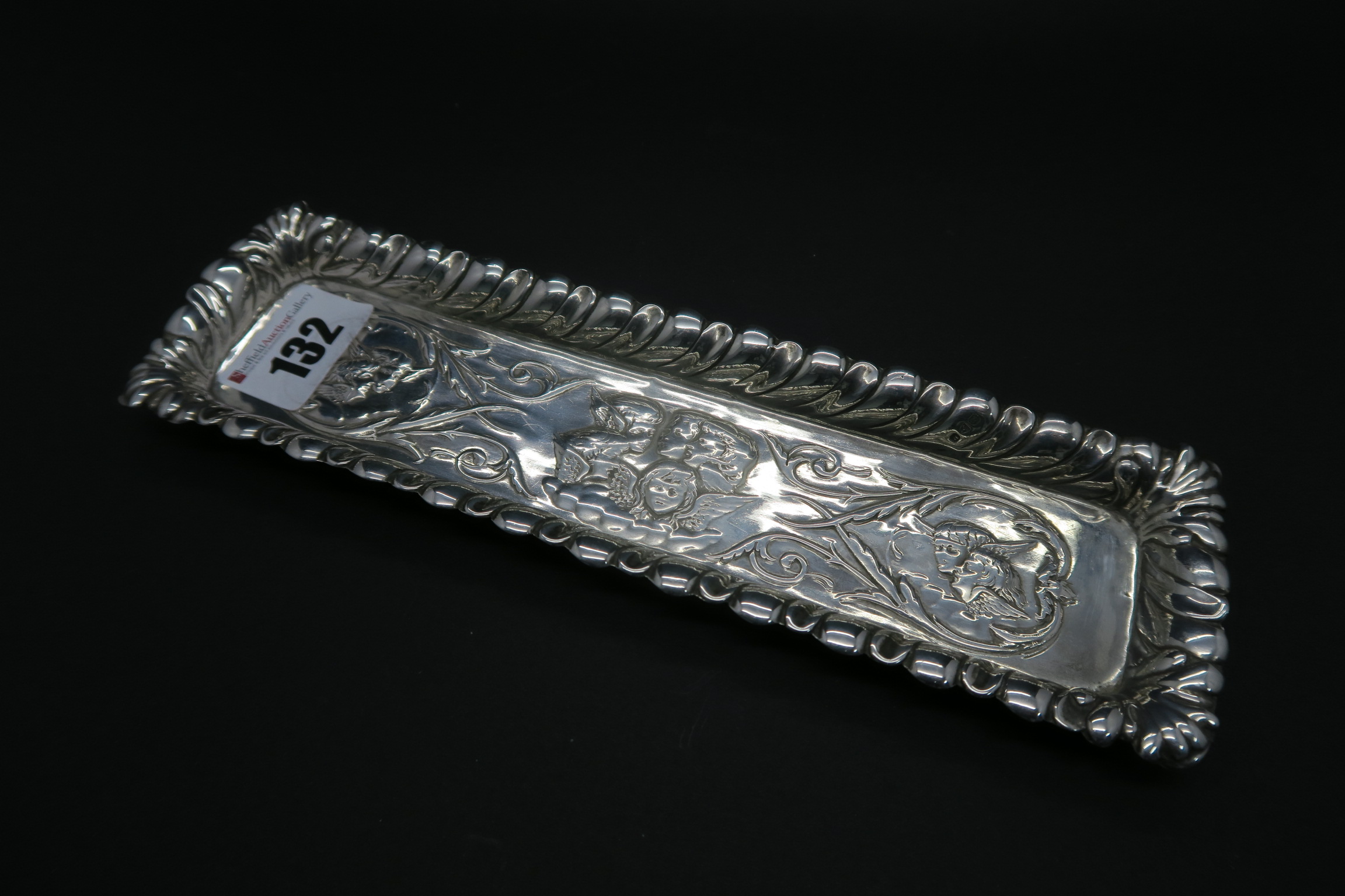 A Chester Hallmarked Silver Pen Tray, 1900, detailed in relief with winged cherubs heads within