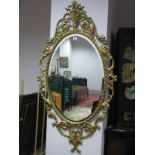 An Oval Bevelled Wall Mirror, in a gilt metal pierced and foliate scrolled frame, feathered effect