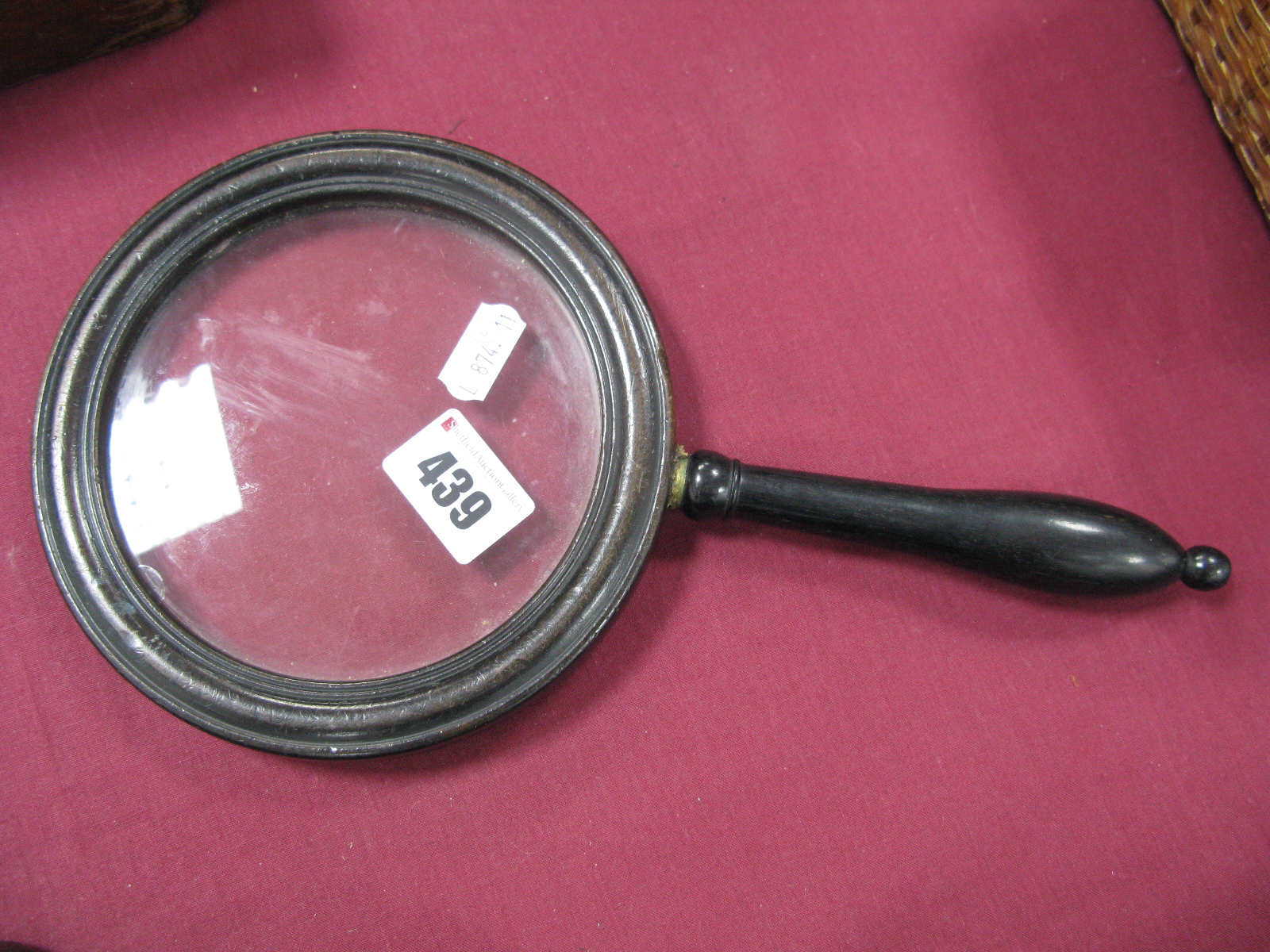 An Ebonised Handled Magnifying Glass, whirl chips to glass interior border, carved wooden nutcracker