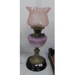 An Oil Lamp, circa 1900 with black glazed terracotta base, lilac tinted glass well and pink shade.