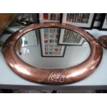 An Arts & Crafts Oval Bevelled Wall Mirror, with four riveted stylised floral motifs to beaten