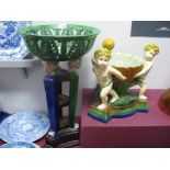 A Majolica Style Wooven and Foliate Basket, supported by three cherubs on raised plinth, and a