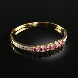 AN 18K YELLOW GOLD, RUBY, AND DIAMOND LADY'S HINGED BANGLE BRACELET, set with a register of