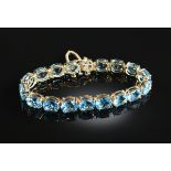 A 14K YELLOW GOLD AND BLUE TOPAZ LADY'S LINE BRACELET, prong set with eighteen oval blue topaz