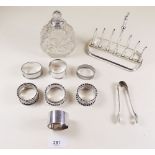 Seven silver napkin rings, a pair of silver sugar tongs 150g total, a cut glass scent bottle with